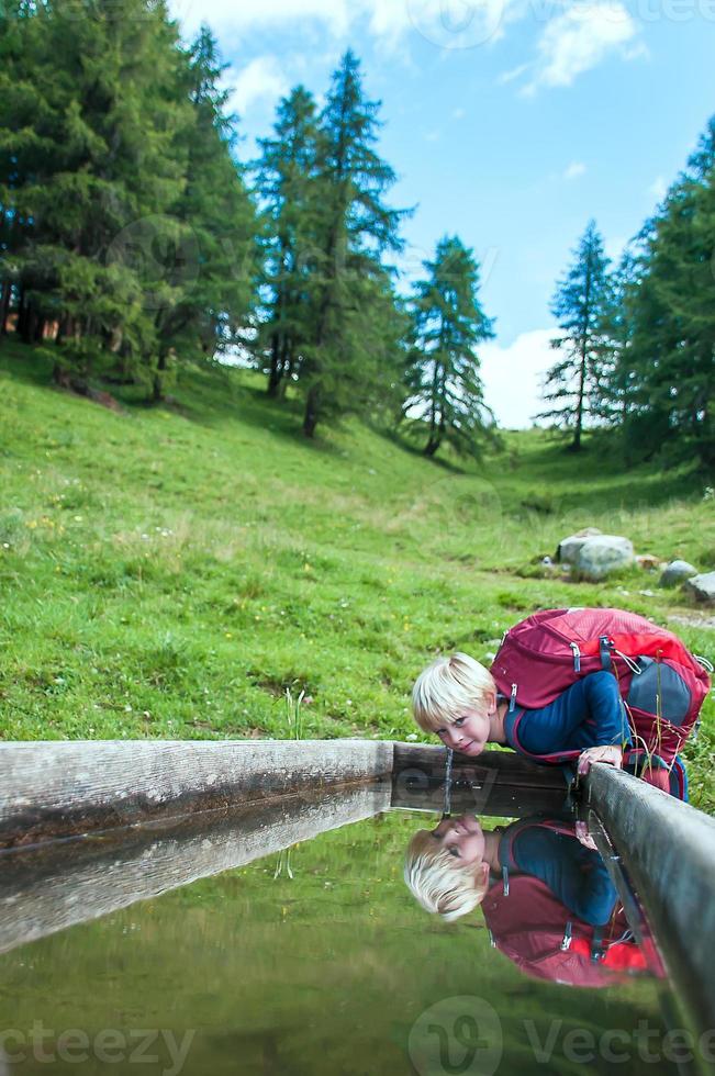 criança bebendo da fonte nas montanhas foto