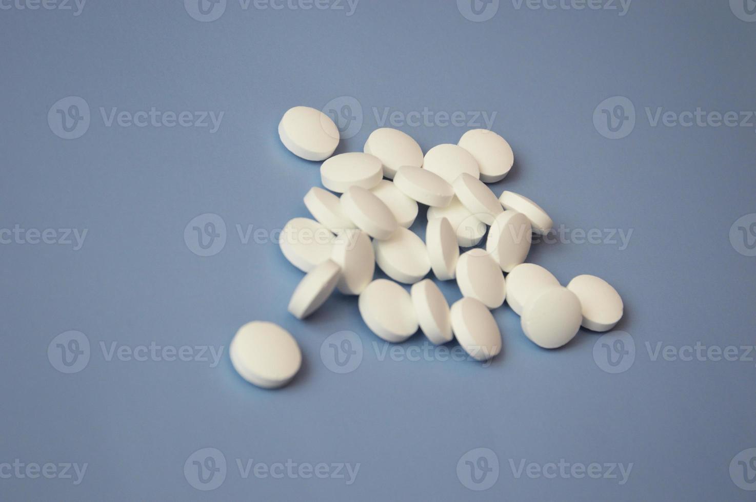 um monte de simples pequenas pílulas brancas redondas espalhadas sobre um fundo azul. close-up, concentre-se em uma pílula. o conceito de medicina, suplementos nutricionais e drogas. espaço livre para texto. foto