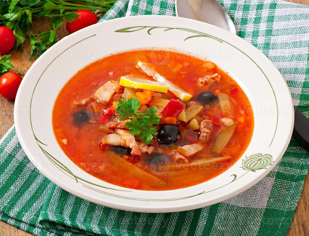 sopa solyanka russo com carne, azeitonas e pepinos em tigela de madeira foto