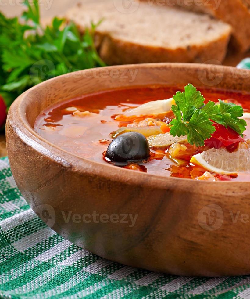 sopa solyanka russo com carne, azeitonas e pepinos em tigela de madeira foto