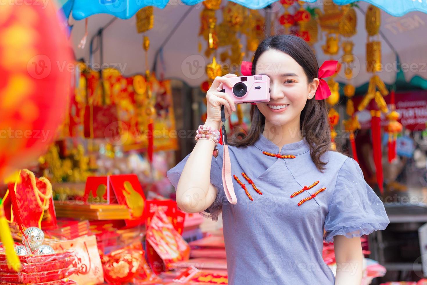 uma linda mulher asiática no vestido qipao azul-cinza segura o saco de pano que exibiu a palavra que significa feliz em chinês e fica na porta de madeira branca como pano de fundo. foto