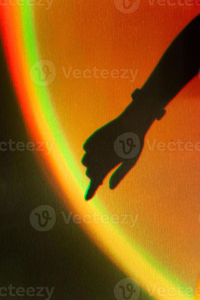 sombra da mão da mulher. reflexo do arco-íris do raio de sol na parede. mão toca arco-íris. foto