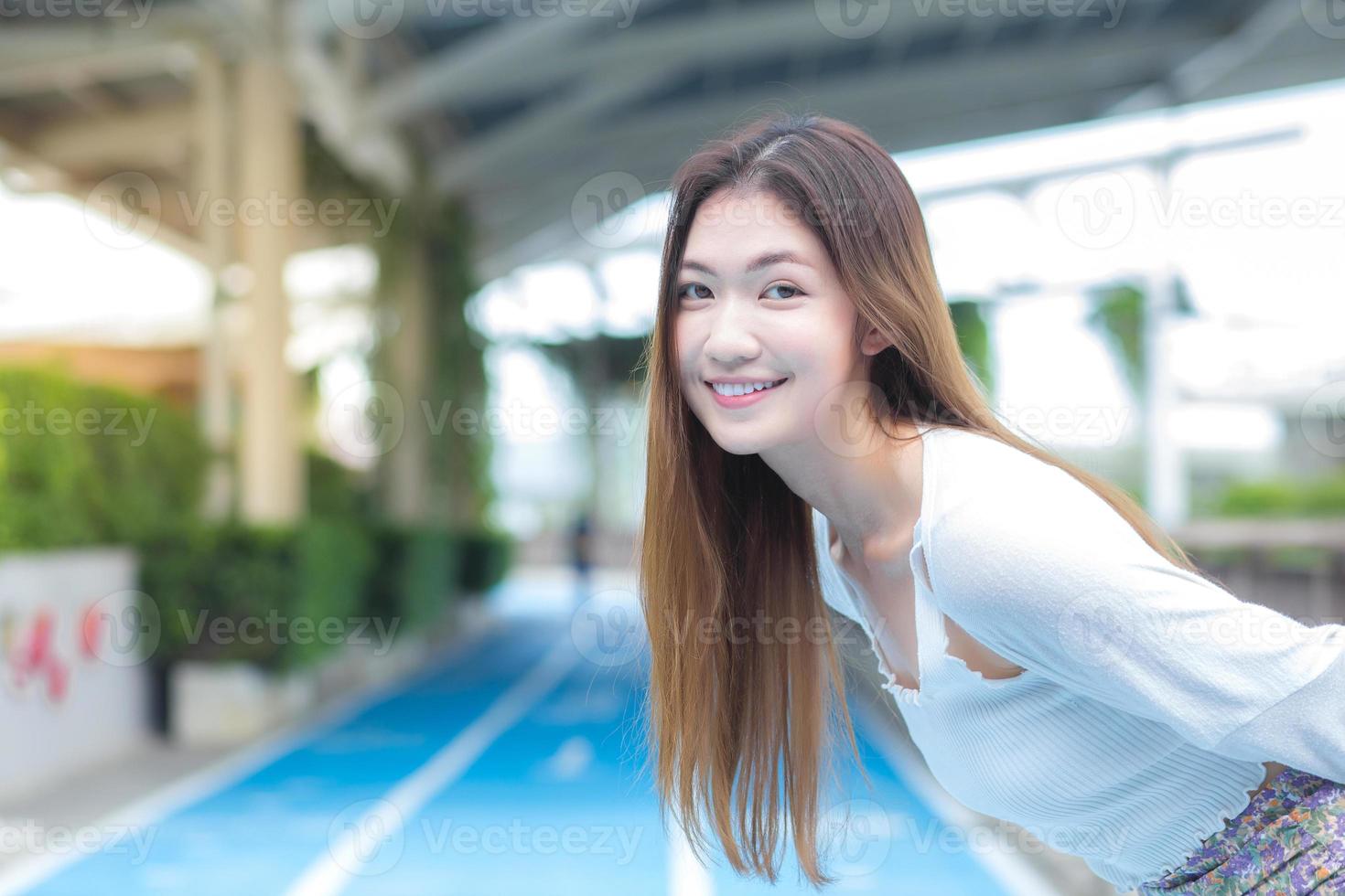 jovem mulher bonita asiática cabelos longos sorrisos brilhantes e fica na esteira ao ar livre da cidade foto