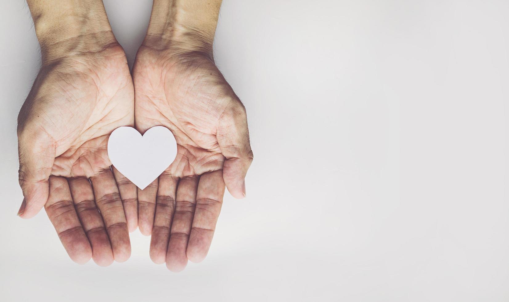 mãos de velho segurando forma de coração em fundo branco. seguro de saúde ou conceito de amor foto