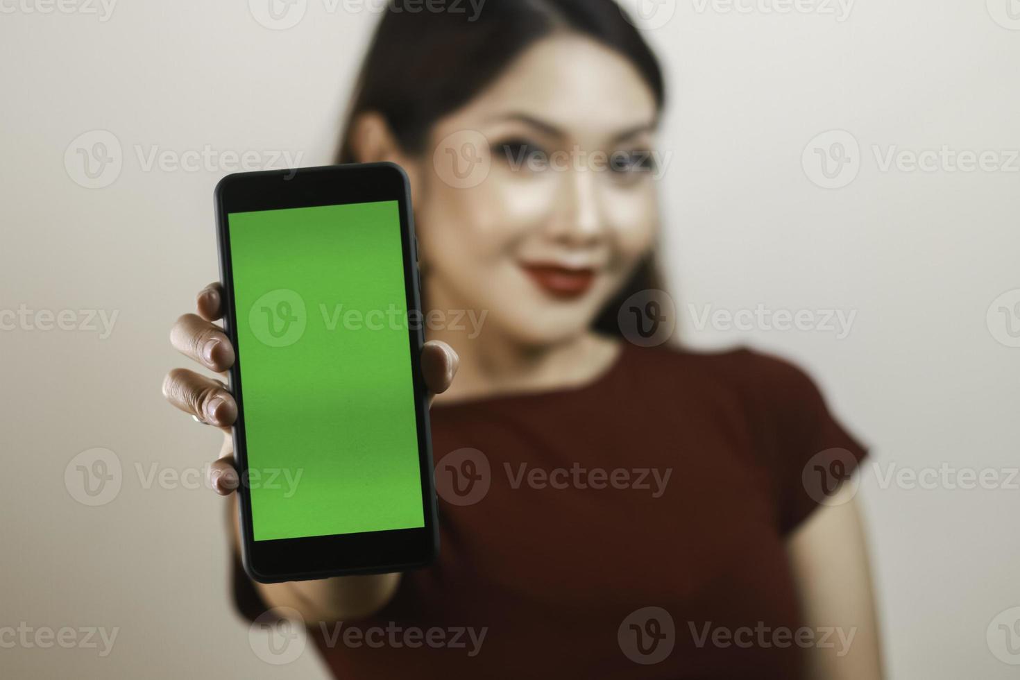 feliz e sorridente jovem asiática mostrando e apontando para uma tela verde em branco. foto