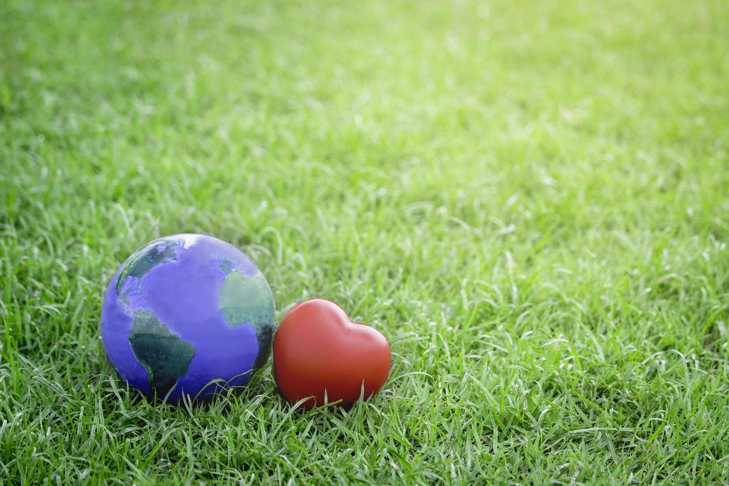 terra com coração vermelho na grama verde, salvar o mundo, amar e proteger nosso planeta e conceito ambientalmente amigável foto