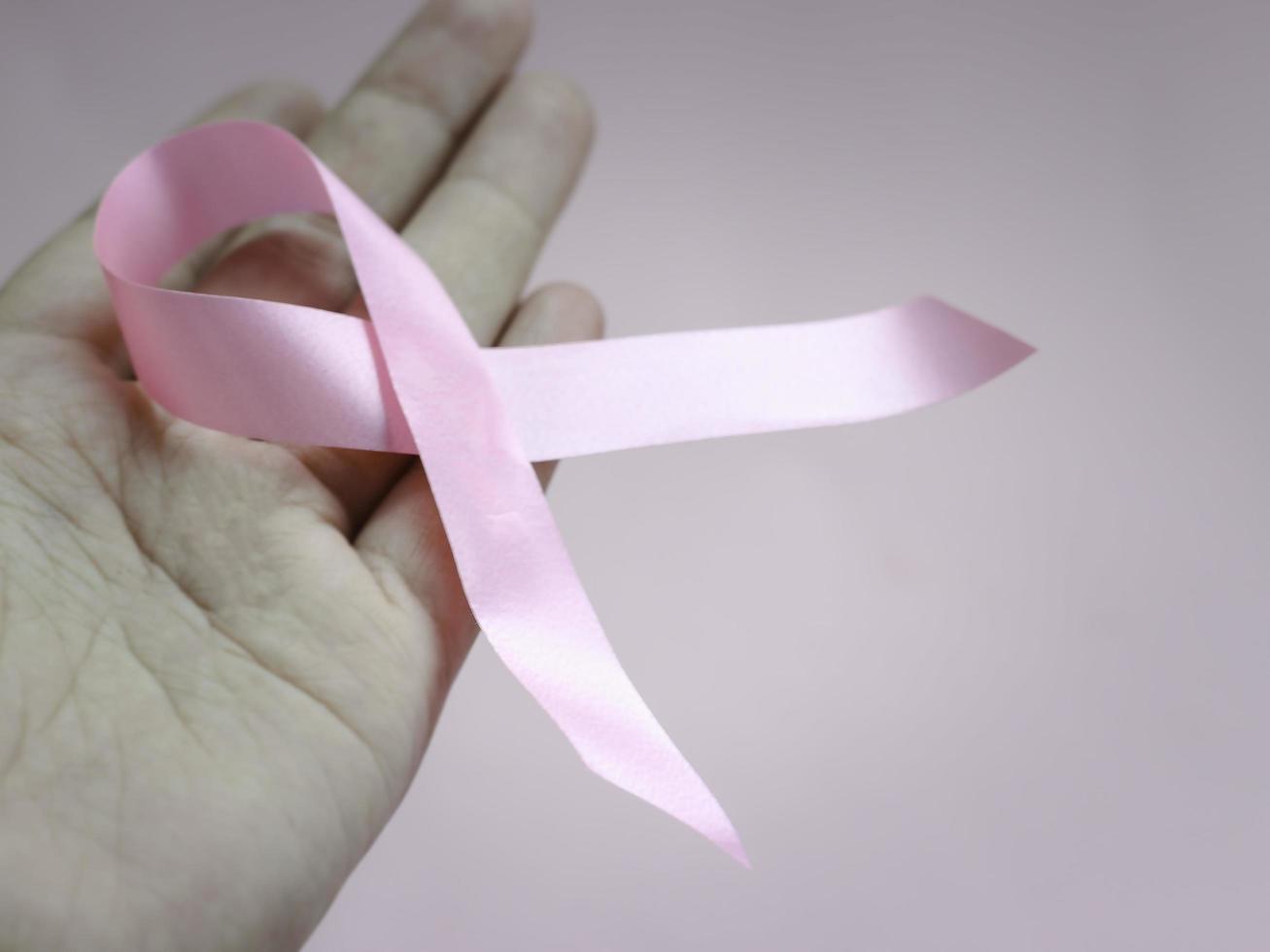 mãos segurando uma fita rosa de conscientização de câncer de mama em fundo rosa, símbolo de outubro, conceito de saúde e medicina foto