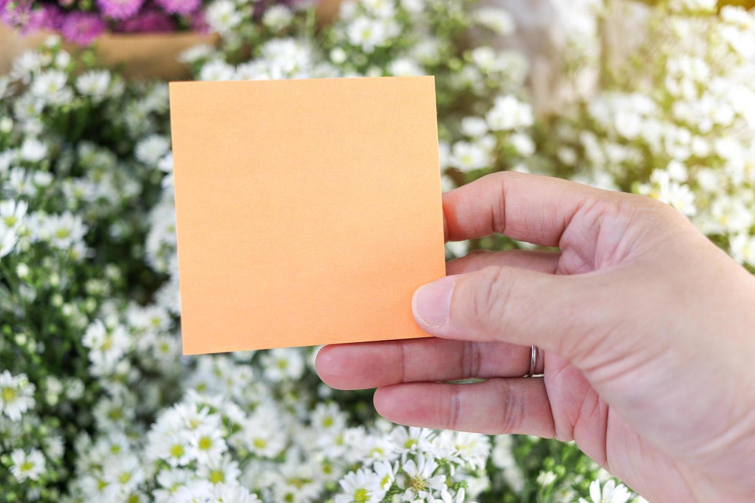 papel de nota em branco na mão sobre fundo de buquê de flores de cortador branco bonito, cópia-espaço no cartão para colocar sua mensagem. foto