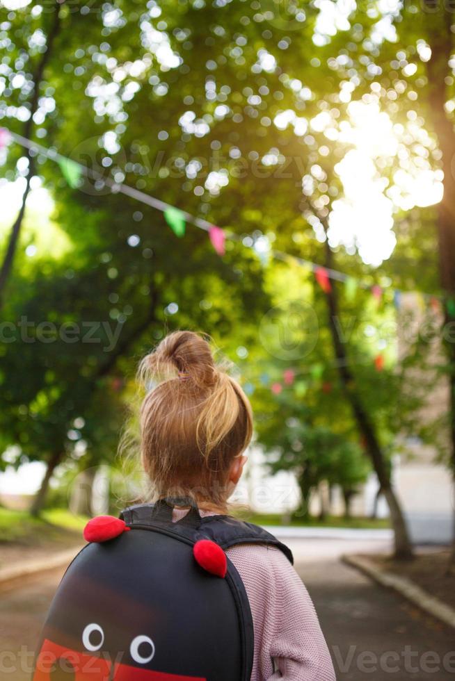 uma garotinha de caucasiano em um uniforme escolar com uma mochila olha para a estrada no pátio da escola. conceito de volta à escola. ensino fundamental, desenvolvendo atividades para pré-escolares. espaço para texto foto