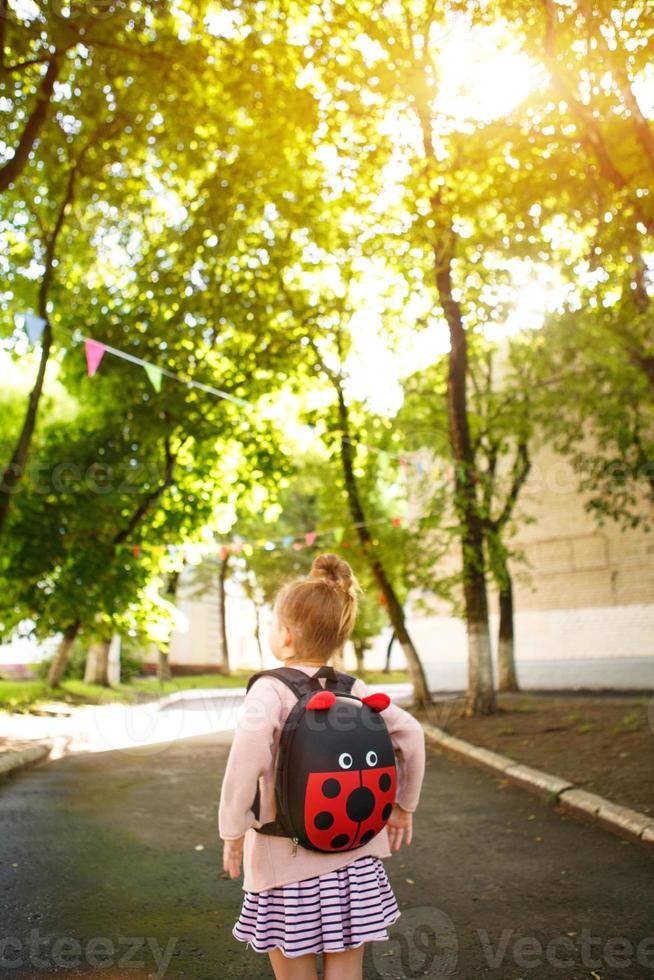 uma garotinha de caucasiano em um uniforme escolar com uma mochila olha para a estrada no pátio da escola. conceito de volta à escola. ensino fundamental, desenvolvendo atividades para pré-escolares. espaço para texto foto