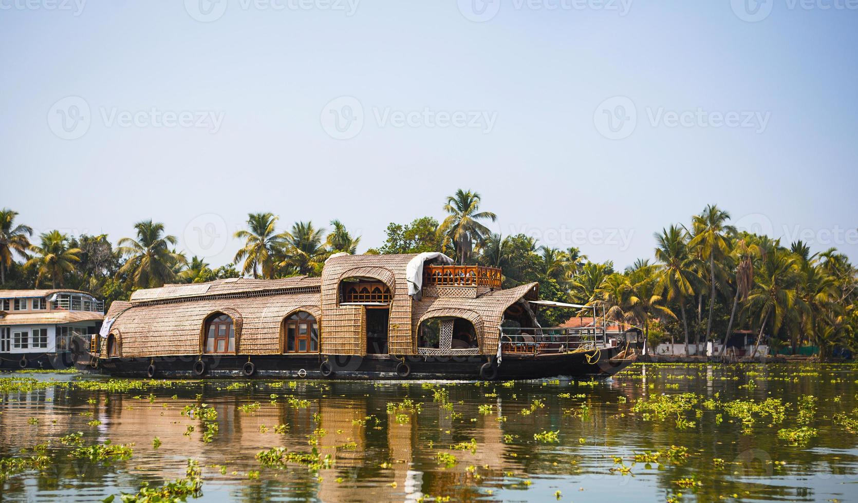 navio de cruzeiro de prazer casa-barco na índia, kerala, nos canais do rio cobertos de algas de allapuzha, na índia. barco no lago sob o sol brilhante e palmeiras entre os trópicos. vista casa-barco foto