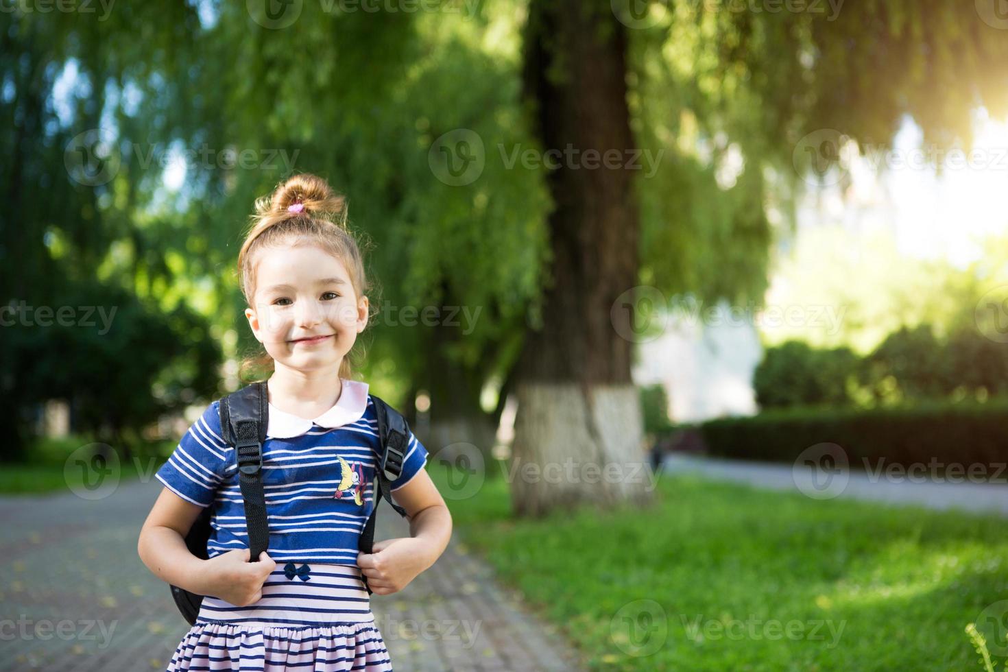 uma garotinha de aparência caucasiana em um uniforme escolar com uma mochila olha para o quadro. conceito de volta à escola. ensino fundamental, desenvolvendo atividades para pré-escolares. espaço para texto foto