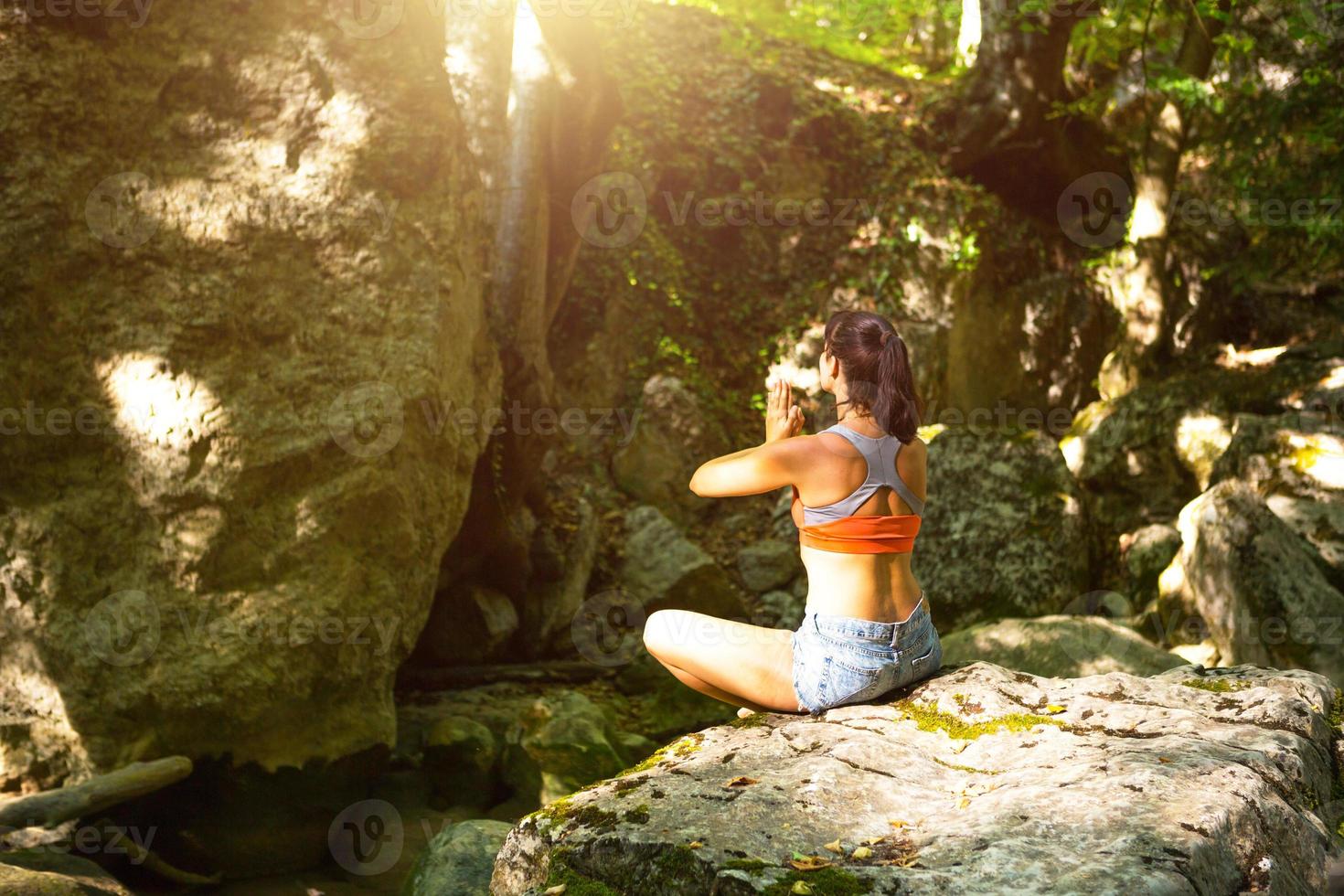 uma mulher senta-se em um campo de lótus em uma grande pedra entre as rochas ao ar livre e medita, desfruta da união com a natureza, ouve o silêncio e os sons da floresta. ecologia foto