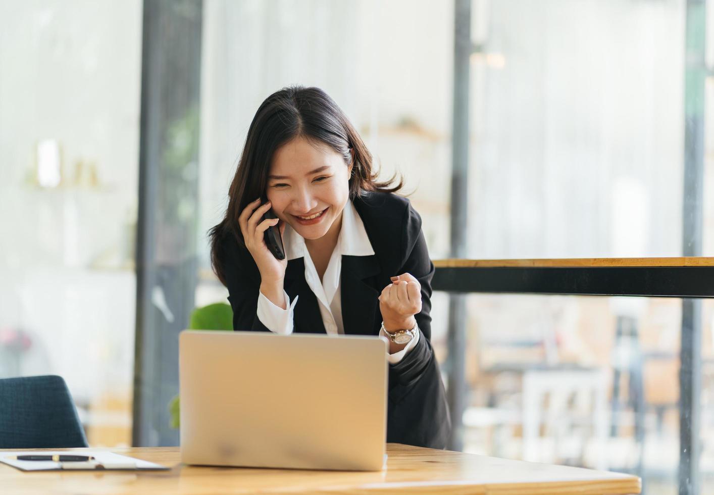 retrato de jovem empresária com terno no café na frente de seu laptop e falando no celular foto