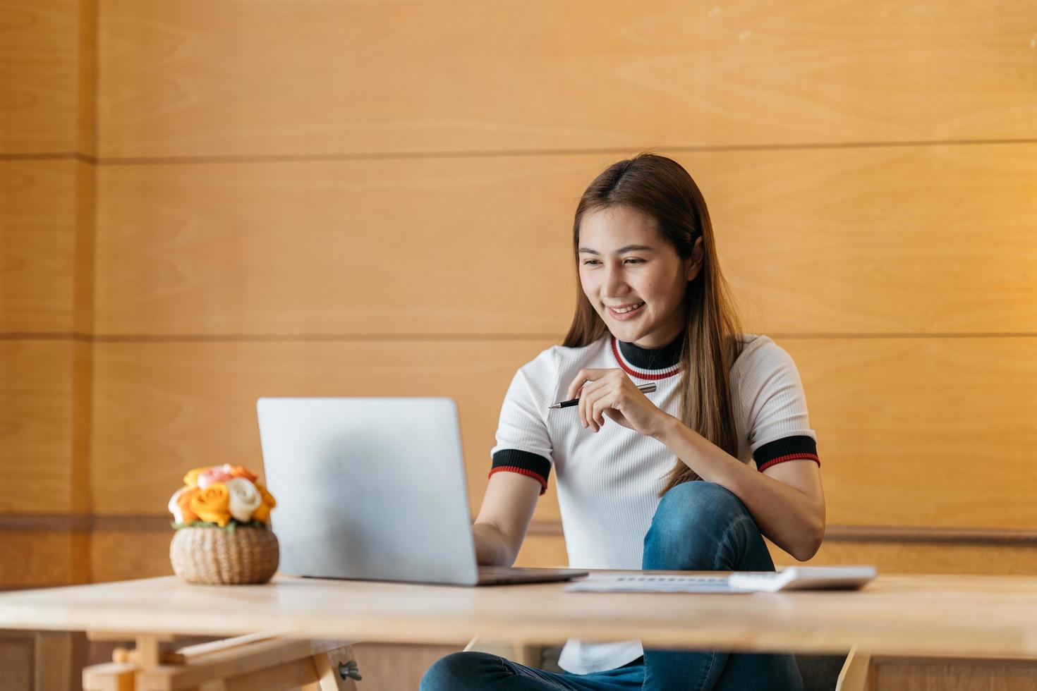 jovem empresária asiática feliz sentado na frente do computador portátil e sorrindo. foto