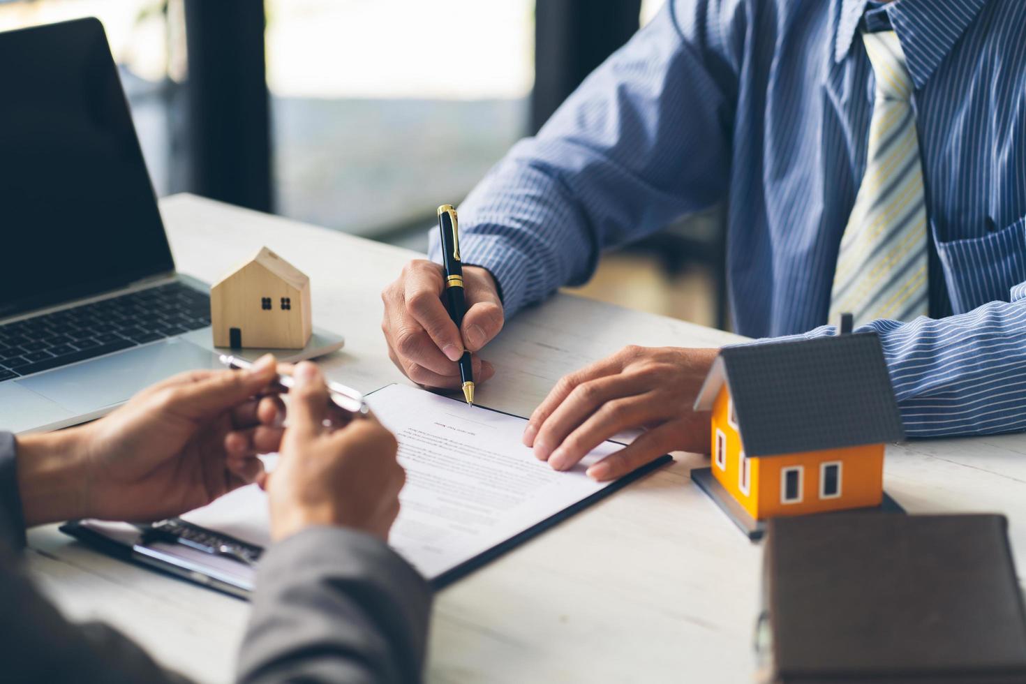 agente imobiliário, ajudando o cliente a assinar o papel do contrato na mesa com o modelo da casa, a agência da casa e o conceito de seguro. foto