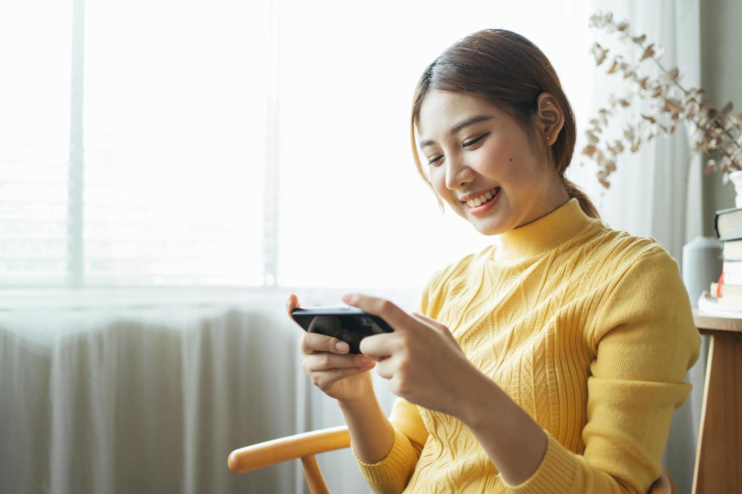 mulher asiática animada enquanto joga jogos para celular, lendo boas notícias enquanto navega no mundo da internet. foto