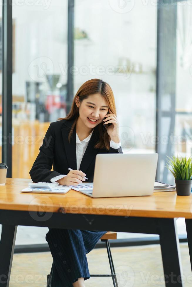 mulher asiática em roupas casuais é feliz e alegre enquanto se comunica com seu smartphone e trabalha em um escritório moderno. foto