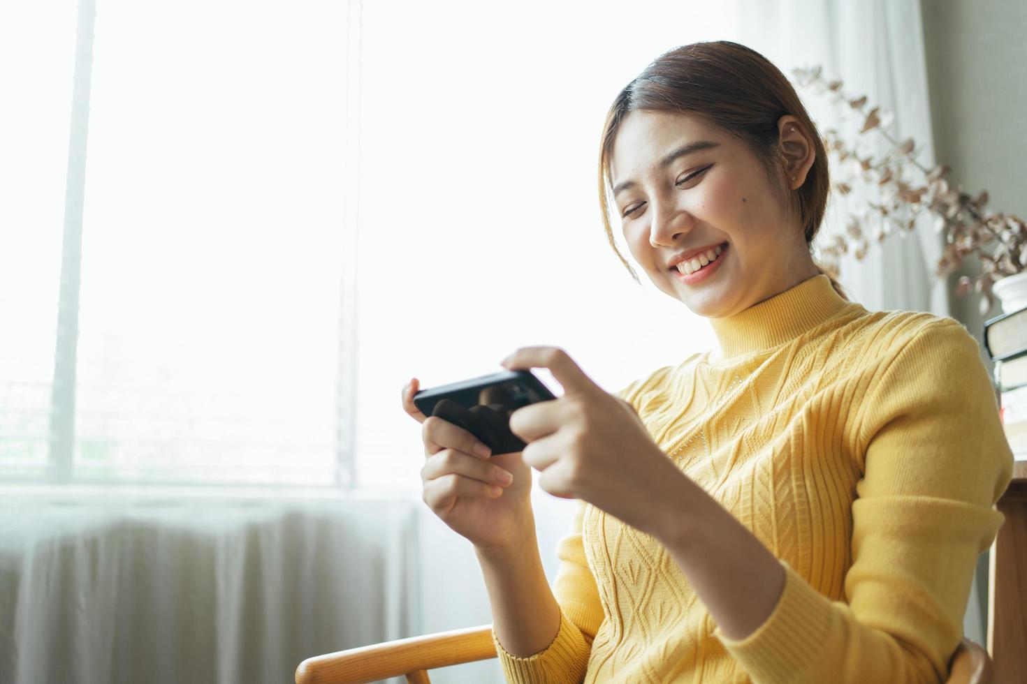 mulher asiática animada enquanto joga jogos para celular, lendo boas notícias enquanto navega no mundo da internet. foto