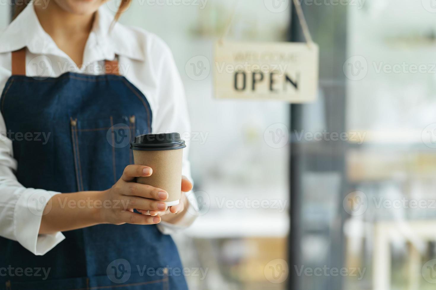 retrato de mulher feliz em pé na porta de sua loja. garçonete madura alegre esperando clientes no café. pequeno empresário bem sucedido em casual vestindo avental azul em pé na entrada foto