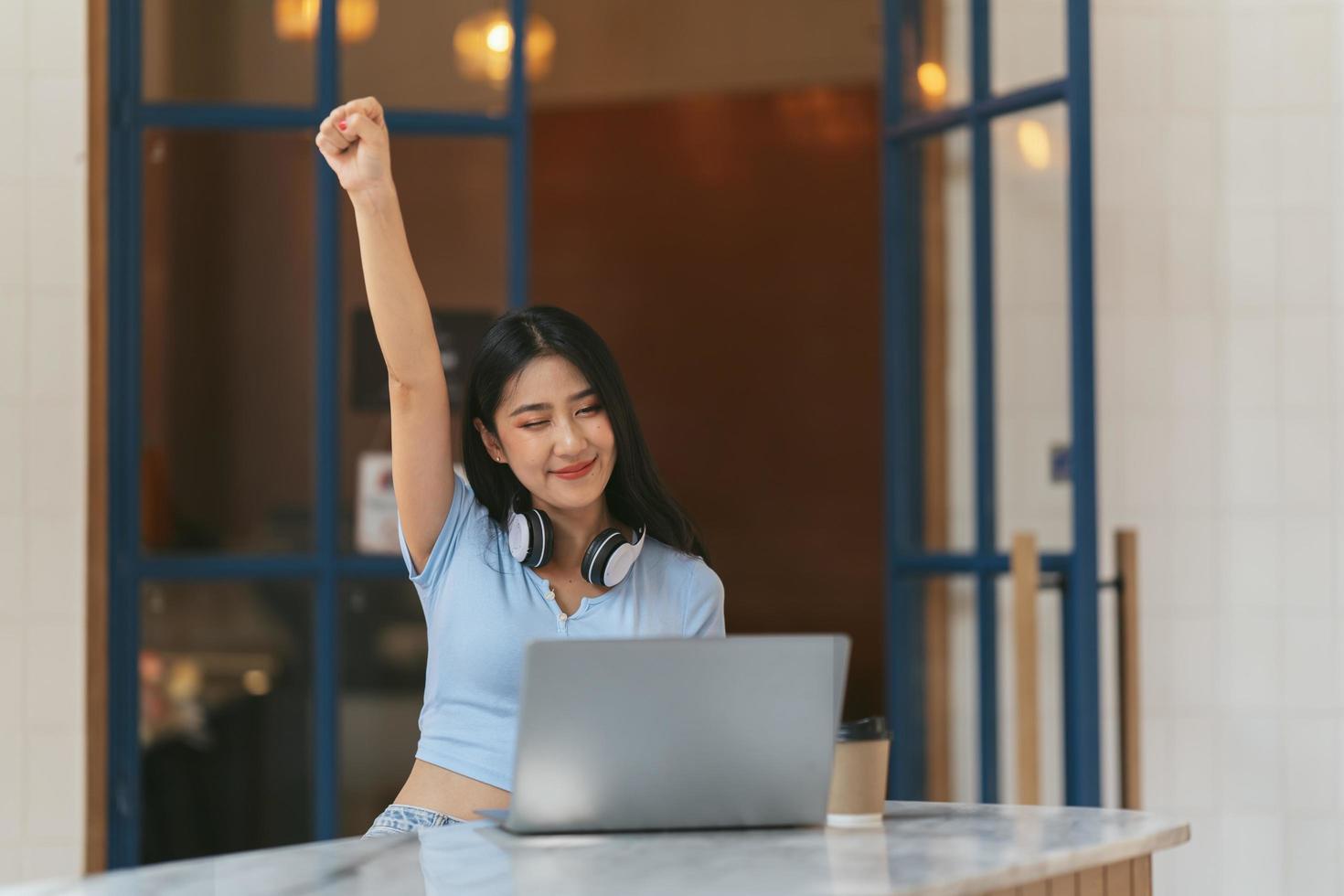 jovem mulher com laptop expressando emoção no escritório em casa, mulher asiática animada se sente eufórica lendo boas notícias online. foto