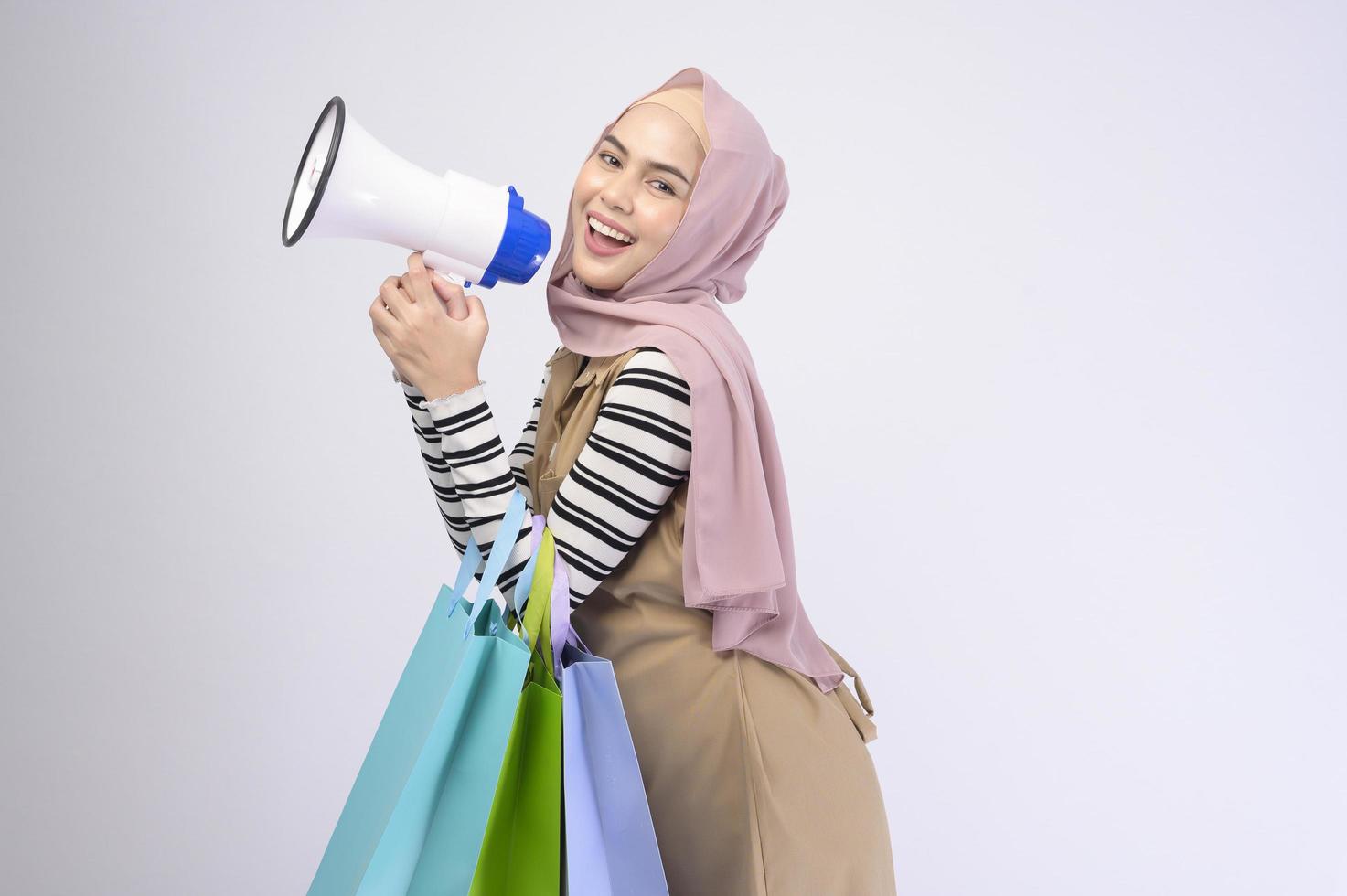 jovem e bela mulher muçulmana de terno segurando sacolas coloridas sobre estúdio de fundo branco foto