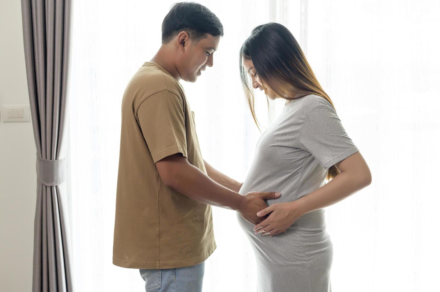 jovem grávida com marido abraçando e esperando um bebê em casa foto