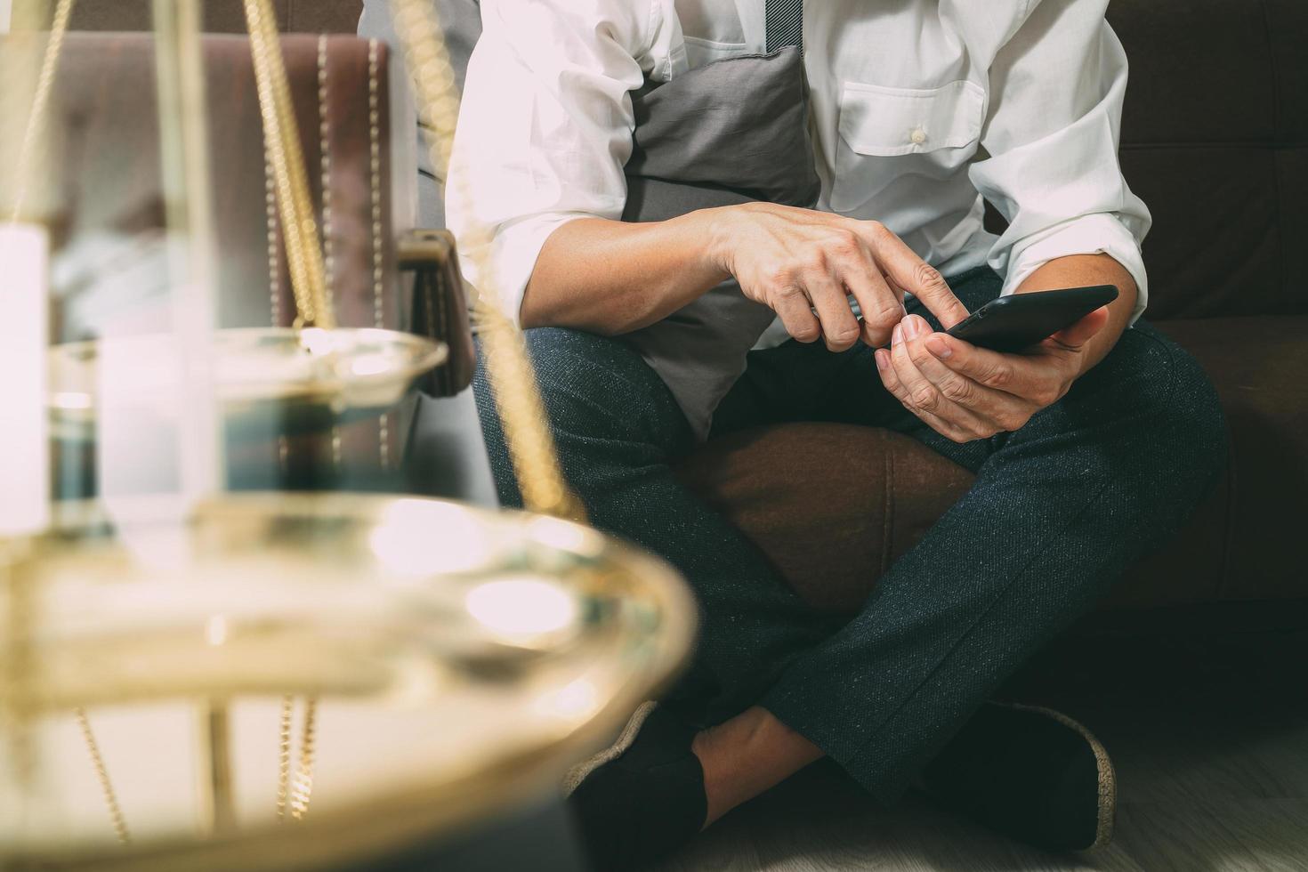 contexto de justiça e lei. mão de advogado masculino sentado no sofá e trabalhando com telefone inteligente, teclado de encaixe de computador tablet digital com martelo e documento na mesa de estar em casa, efeito de filtro foto