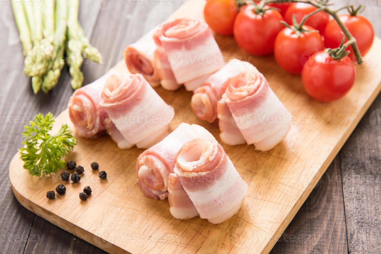 rolos de bacon com tomate, aspargos em fundo de madeira foto