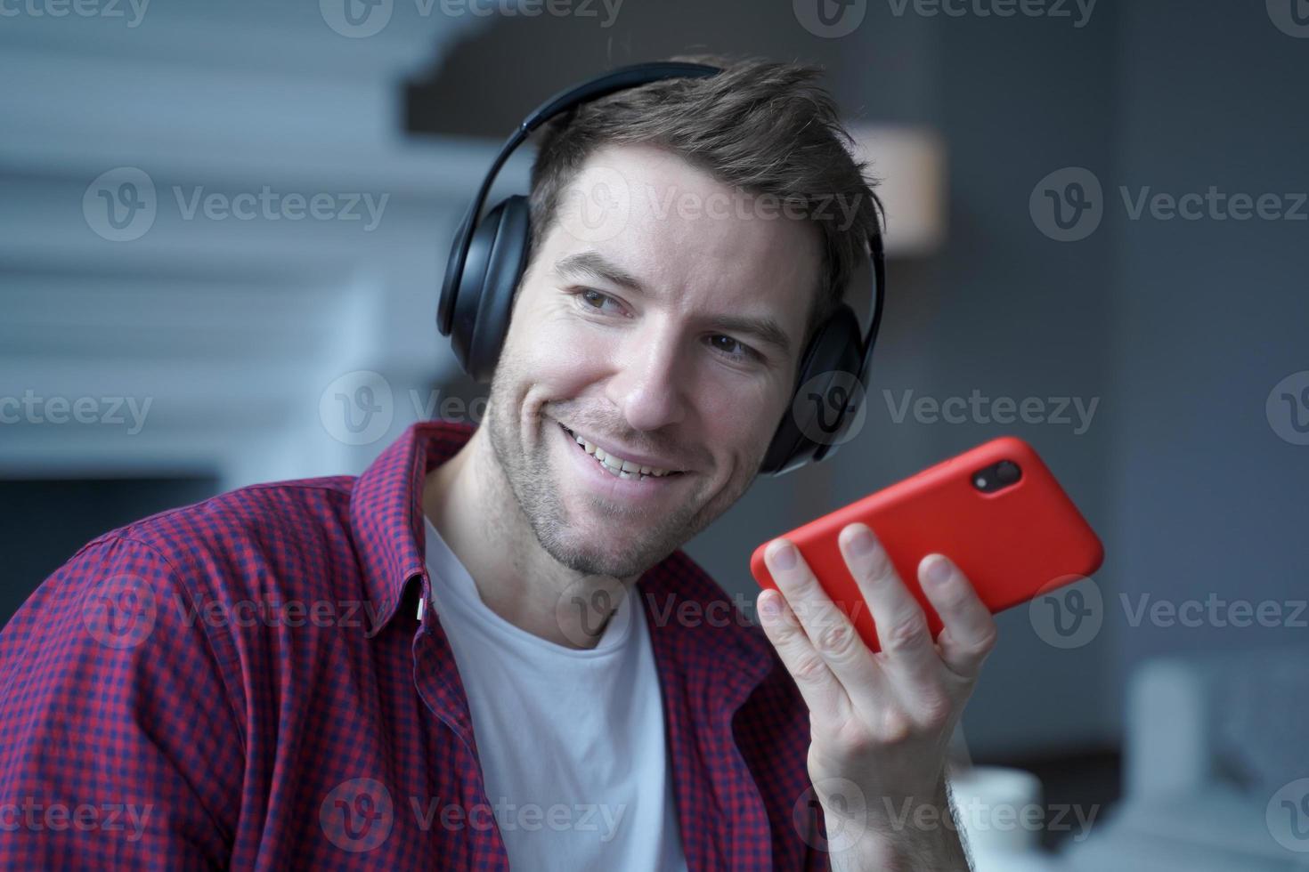 sorrindo jovem alemão em fones de ouvido gravando mensagem de voz para colega, usando viva-voz foto