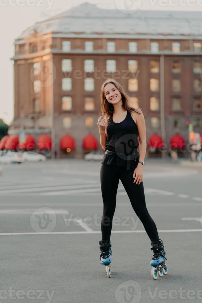 tiro de corpo inteiro de mulher sorridente ativa gosta de passeios de esportes radicais em patins vestidos com roupas confortáveis pretas fica ao ar livre aprende patins. conceito de recreação de lazer de pessoas foto