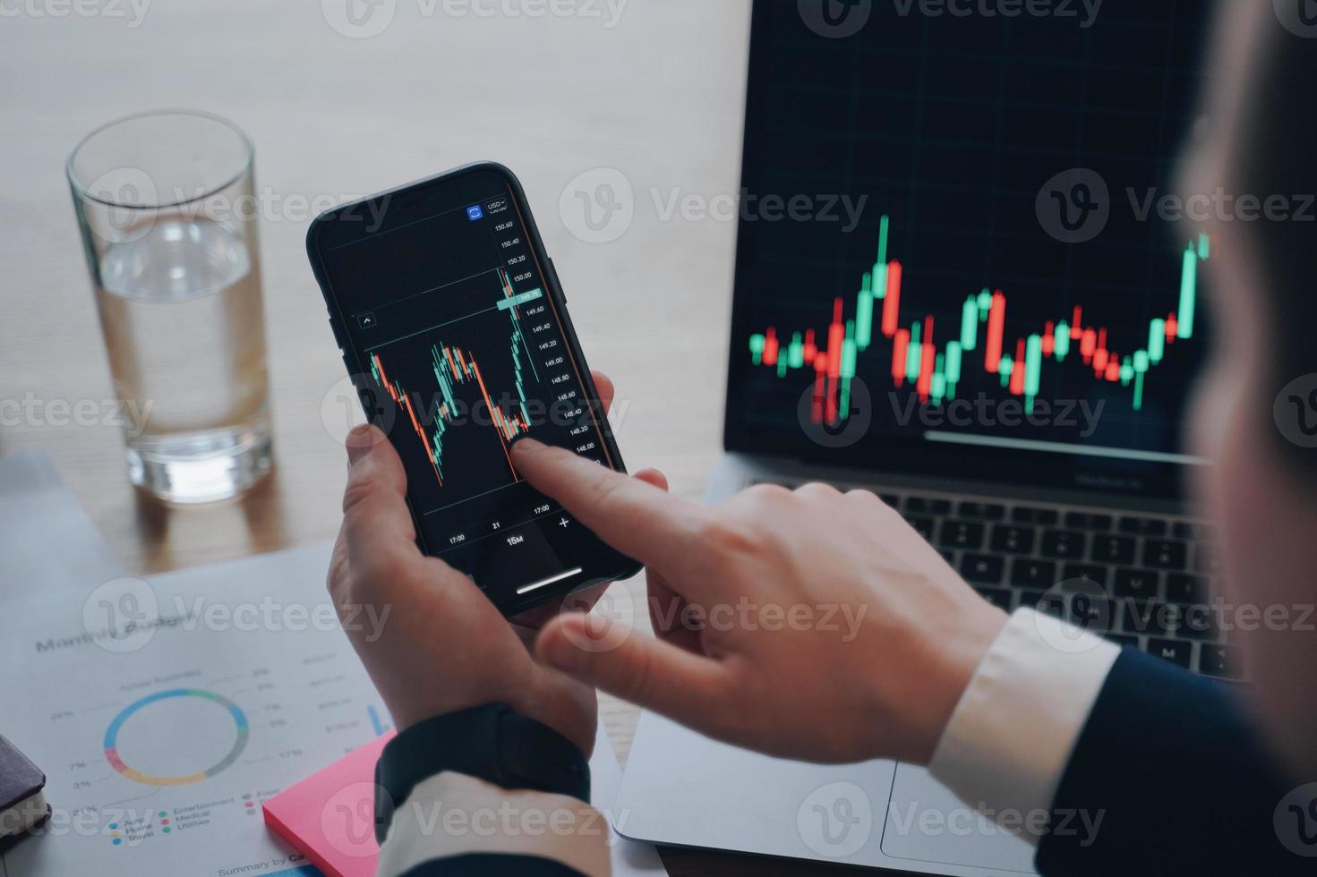 gráfico financeiro no laptop. homem clica com o dedo na tela do telefone. negociação e investimento online. foto