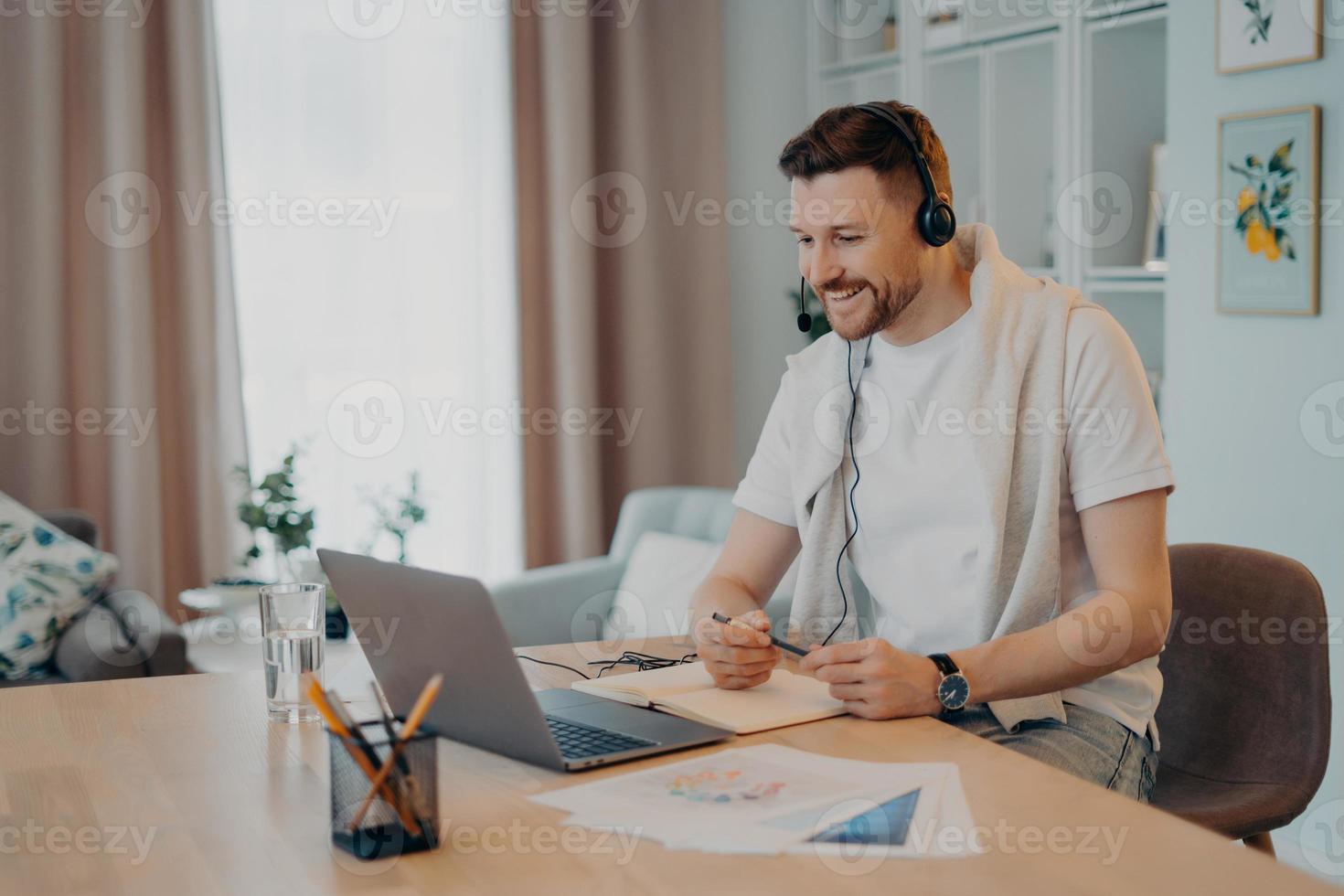 jovem macho sorridente no fone de ouvido estudando em casa durante a quarentena foto
