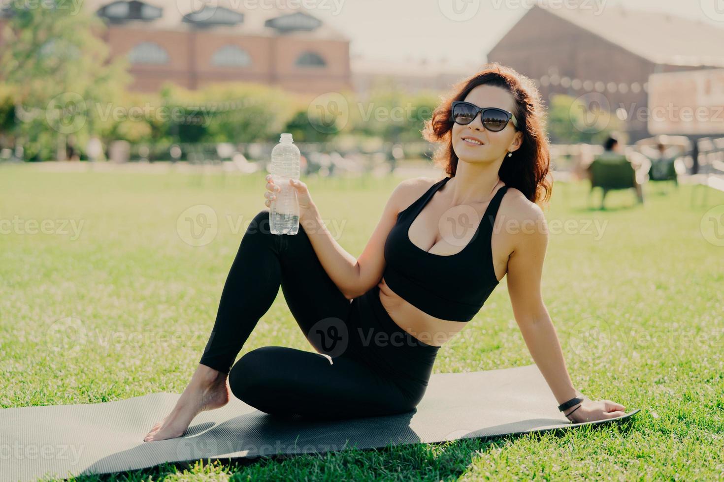 mulher ativa positiva tem forma corporal perfeita como resultado de poses regulares de treinamento físico no karemat com garrafa de água descansa após o treino passa o tempo livre ao ar livre. praticando ioga de manhã foto