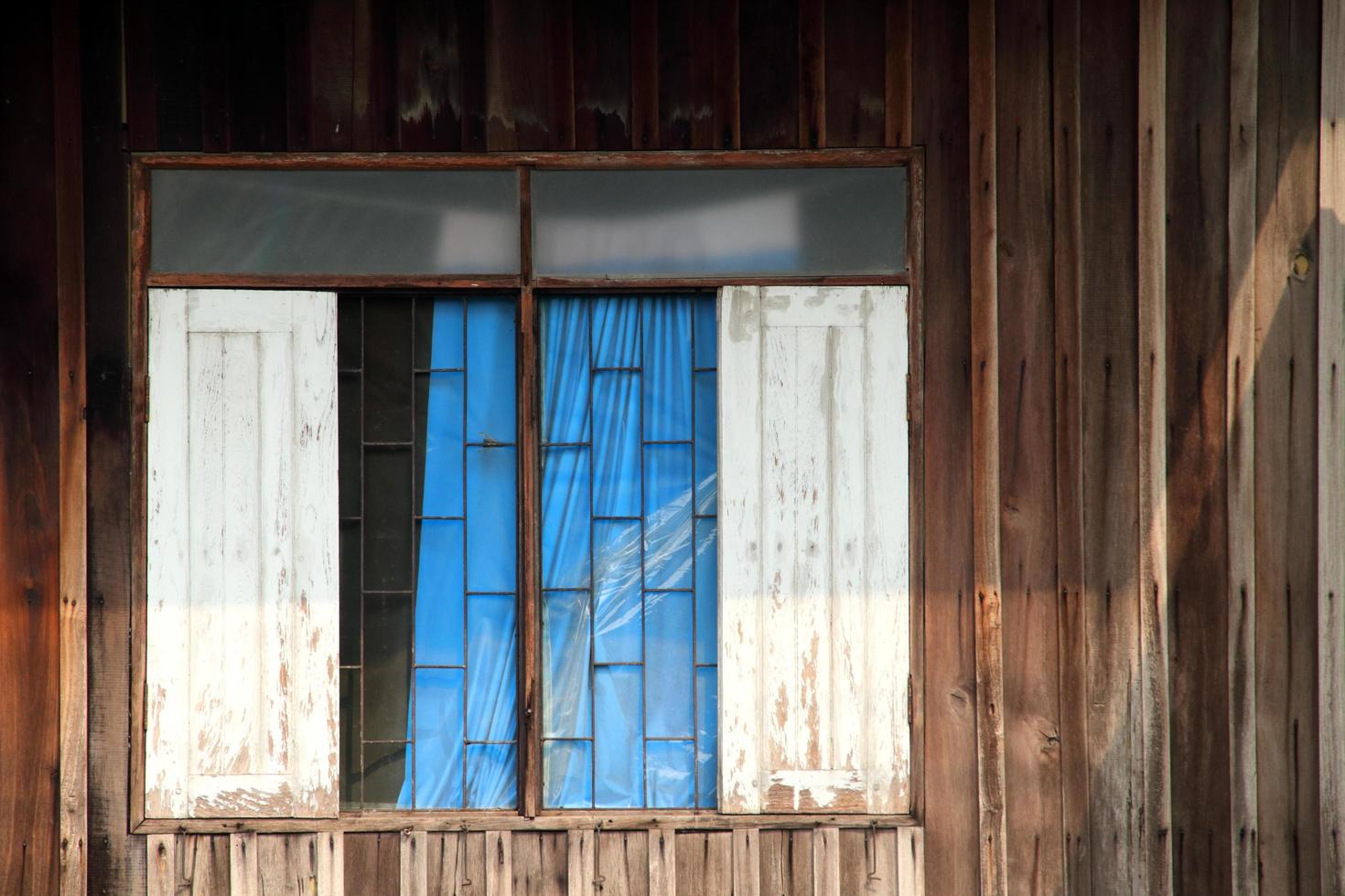 janela de madeira branca em estilo retro, parede de madeira velha aberta e escura, cortina azul brilhante dentro de casa na tailândia. foto