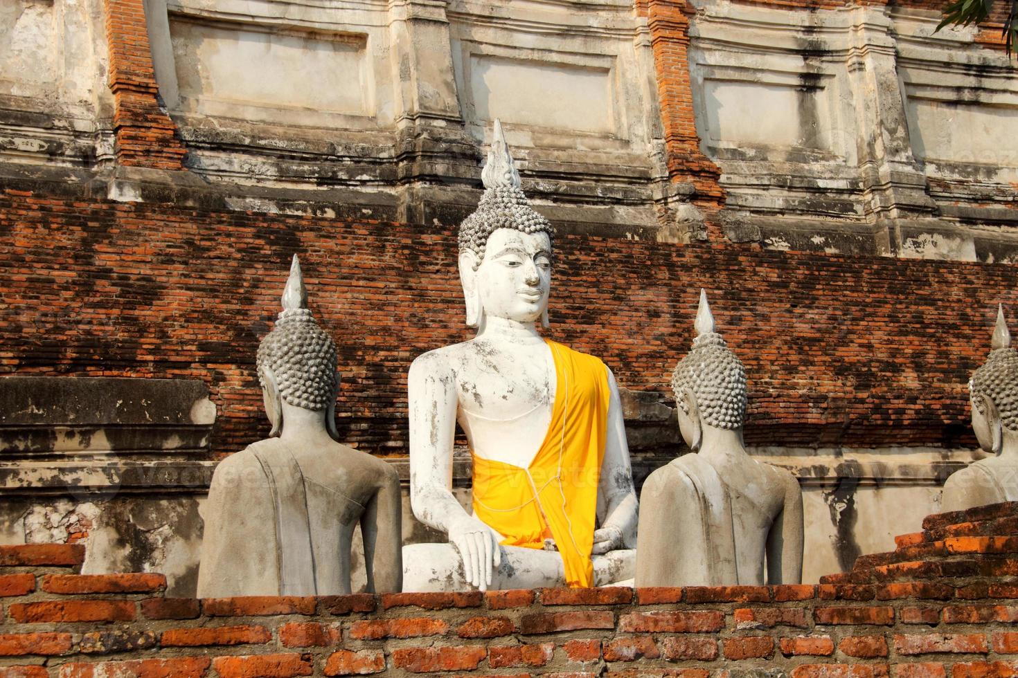 estátua de buda pintada de branco coberta de pano amarelo com parede de tijolo vermelho quebrada na frente e fundo no templo, província de ayutthaya, tailândia. foto