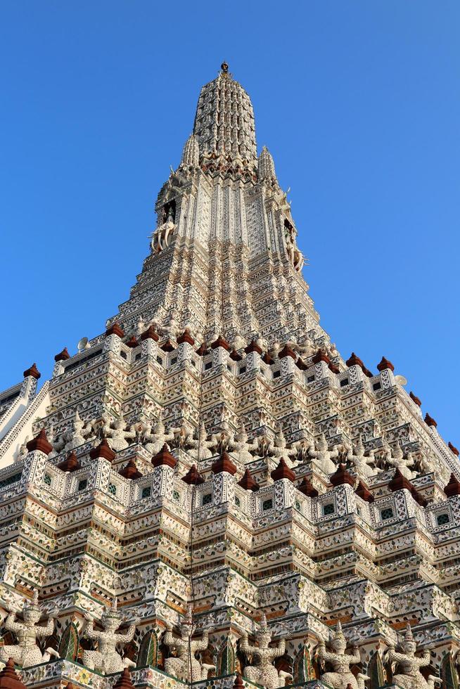 pagode branco no templo de wat arun e céu azul. estátuas antigas em torno da base do pagode. Wat Arun é um monumento antigo na Tailândia. foto