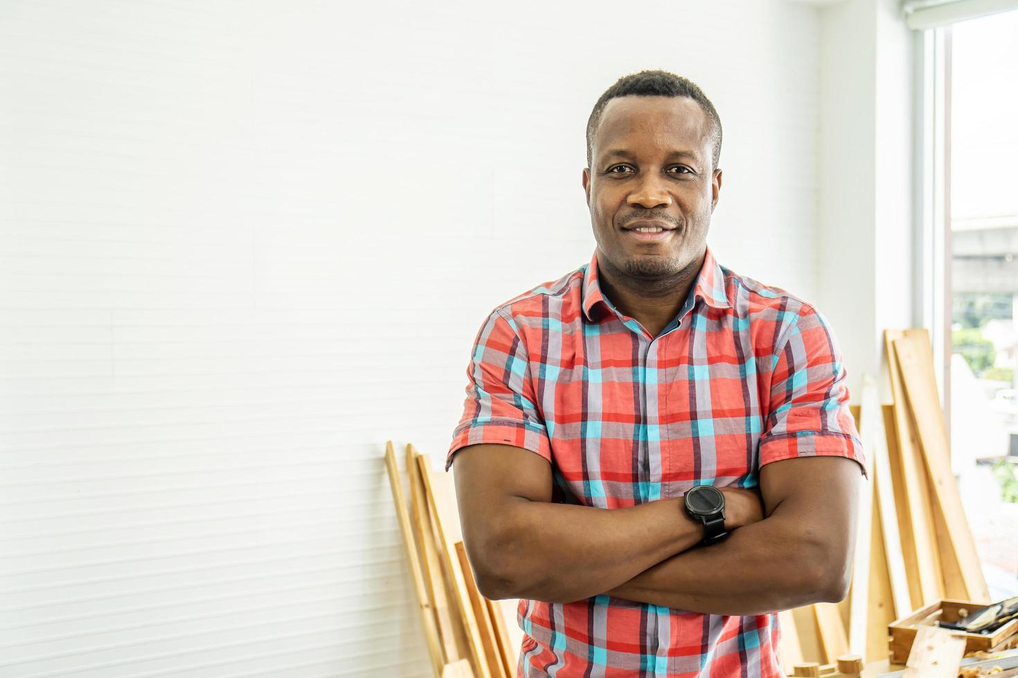 retrato afro-americano feliz marceneiro ou carpinteiro sorrindo, vestindo camisa cruzando os braços para criar móveis de madeira diy como hobby foto