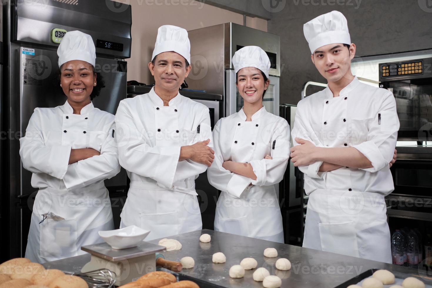 um grupo de funcionários da equipe de chefs felizes profissionais multirraciais em uniformes de cozinha brancos fica em uma fileira, braços cruzados com confiança, sorrisos alegres com trabalhos de culinária comercial na cozinha do restaurante. foto