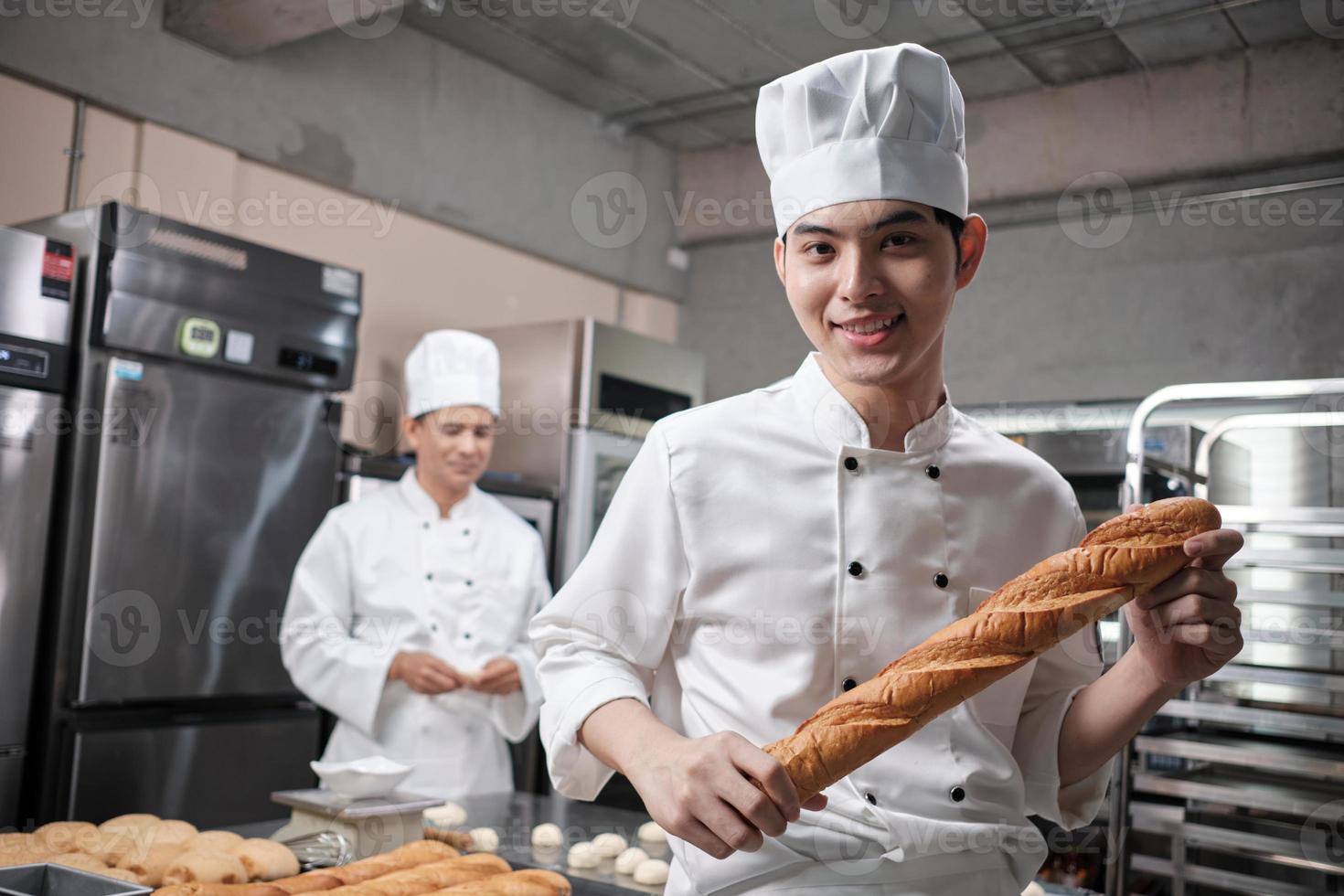 retrato do jovem chef masculino asiático em uniforme de cozinha branco parece câmera, sorriso feliz e alegre com baguete, ocupação de alimentos profissionais, trabalhos de culinária de pastelaria comercial em uma cozinha de restaurante. foto