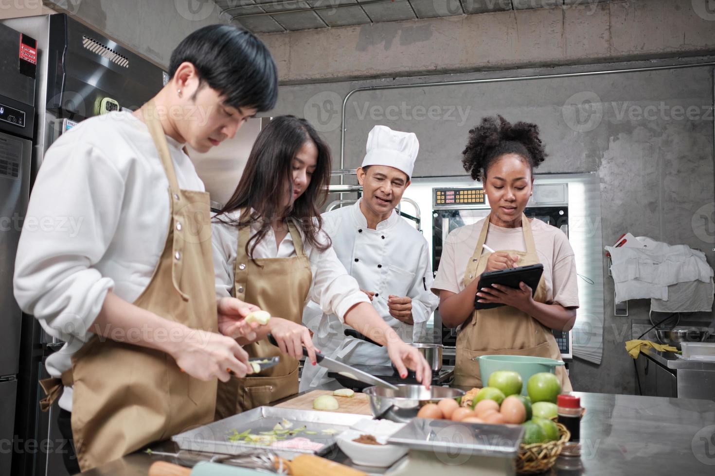 curso de culinária de hobby, chef masculino sênior em uniforme de cozinheiro ensina jovens estudantes de culinária a descascar e picar maçãs, ingredientes para alimentos de pastelaria, tortas de frutas na cozinha de aço inoxidável do restaurante. foto