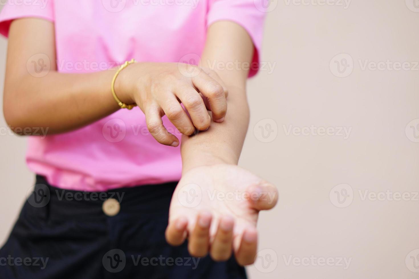 mulher coçando o braço de coceira no fundo cinza claro. causa de coceira na pele incluem picadas de insetos conceito de cuidados de saúde da pele. foto