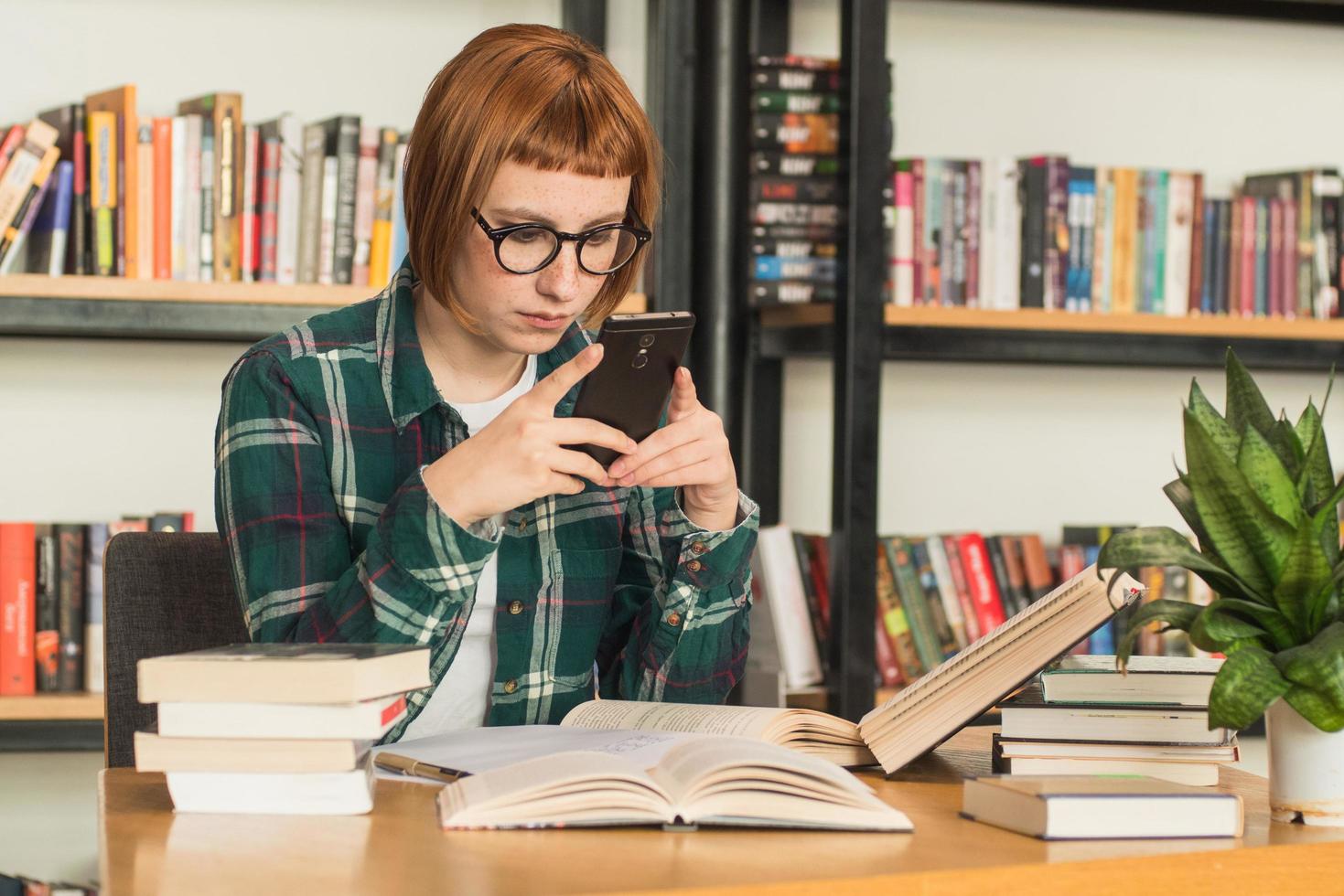 mulher jovem ruiva de óculos ler livro na biblioteca foto