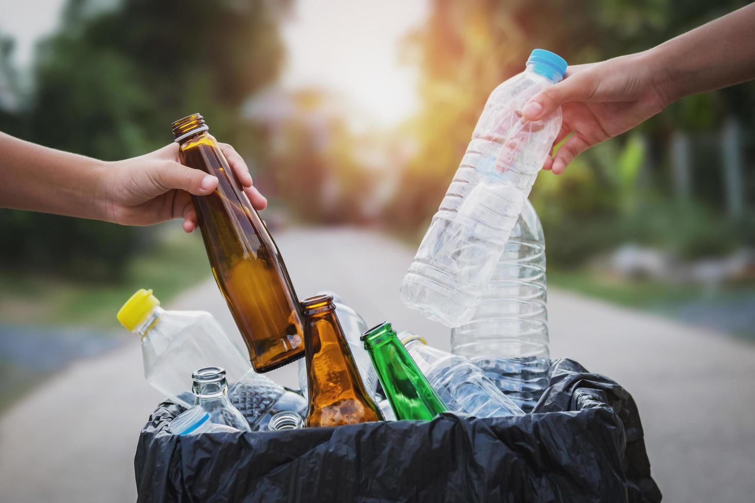 mão de pessoas segurando plástico de garrafa de lixo e vidro colocando em saco de reciclagem para limpeza foto