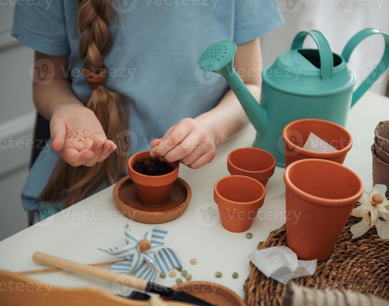 menina sentada à mesa em casa, semeando sementes em vasos de flores. foto