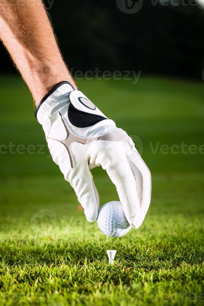 mão segure a bola de golfe com tee no curso foto