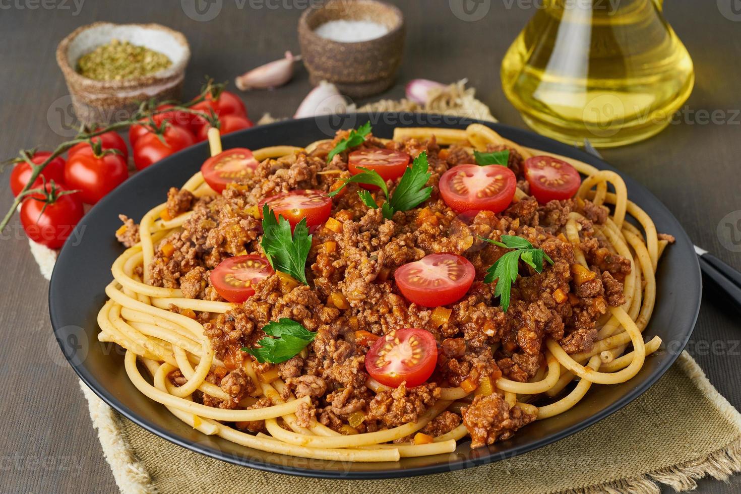 macarrão à bolonhesa bucatini com carne moída e tomate, fundo escuro de madeira, closeup foto