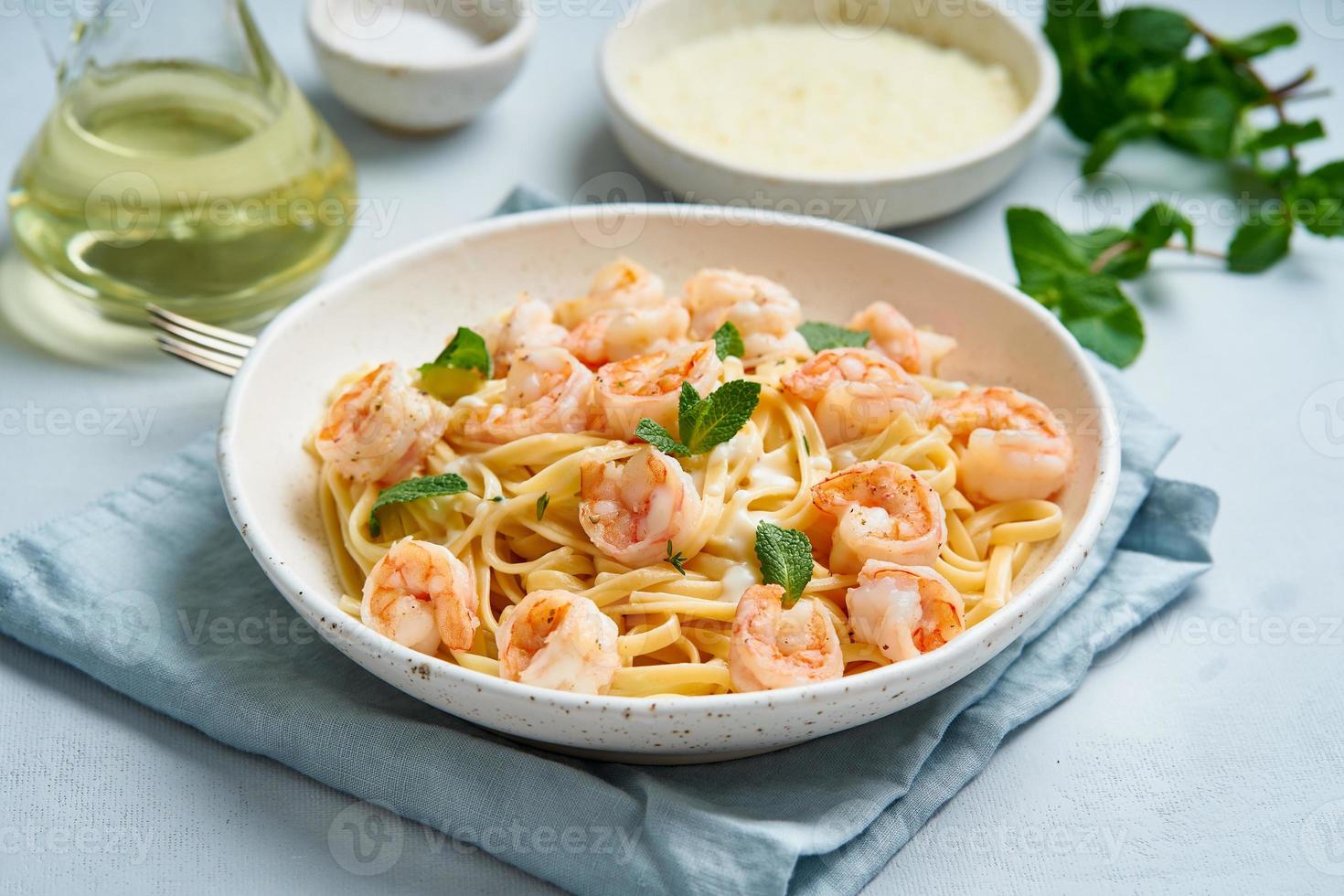 macarrão espaguete com camarões grelhados, molho bechamel, folha de hortelã na mesa azul foto