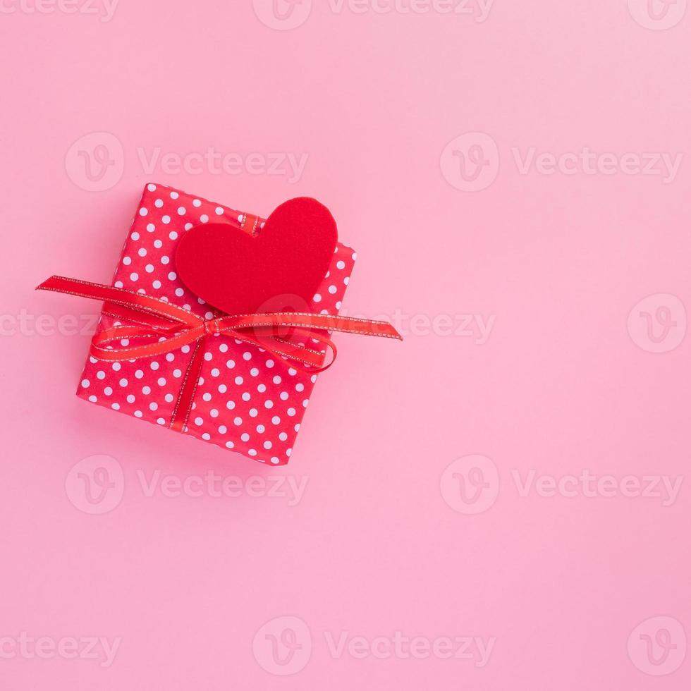 presente na caixa de presente vermelha com laço, coração vermelho, fundo rosa, vista superior, espaço vazio para texto. foto