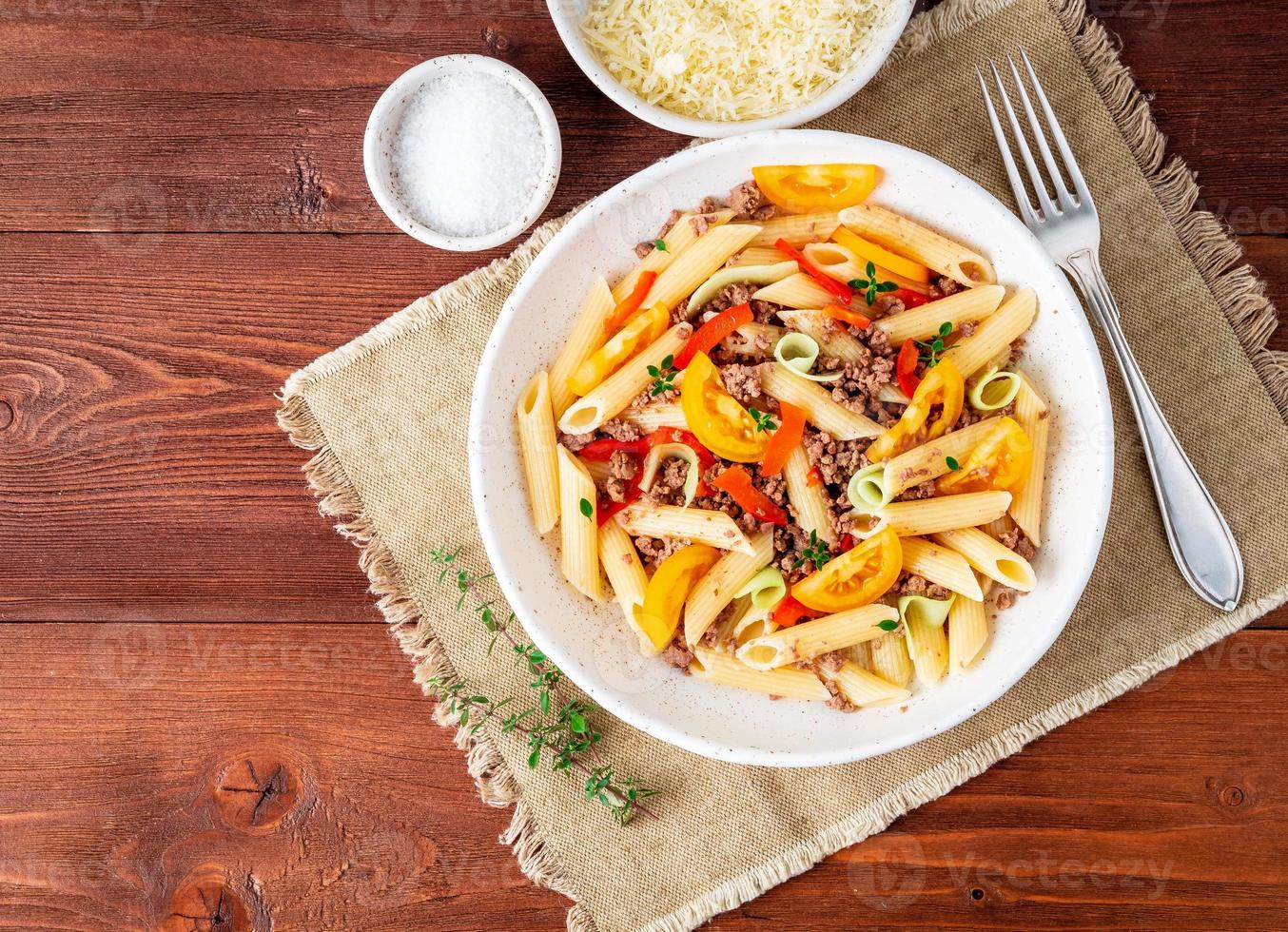 macarrão penne com tomate amarelo, legumes vermelhos e verdes, picadinho no fundo escuro de madeira, vista superior, copie o espaço foto